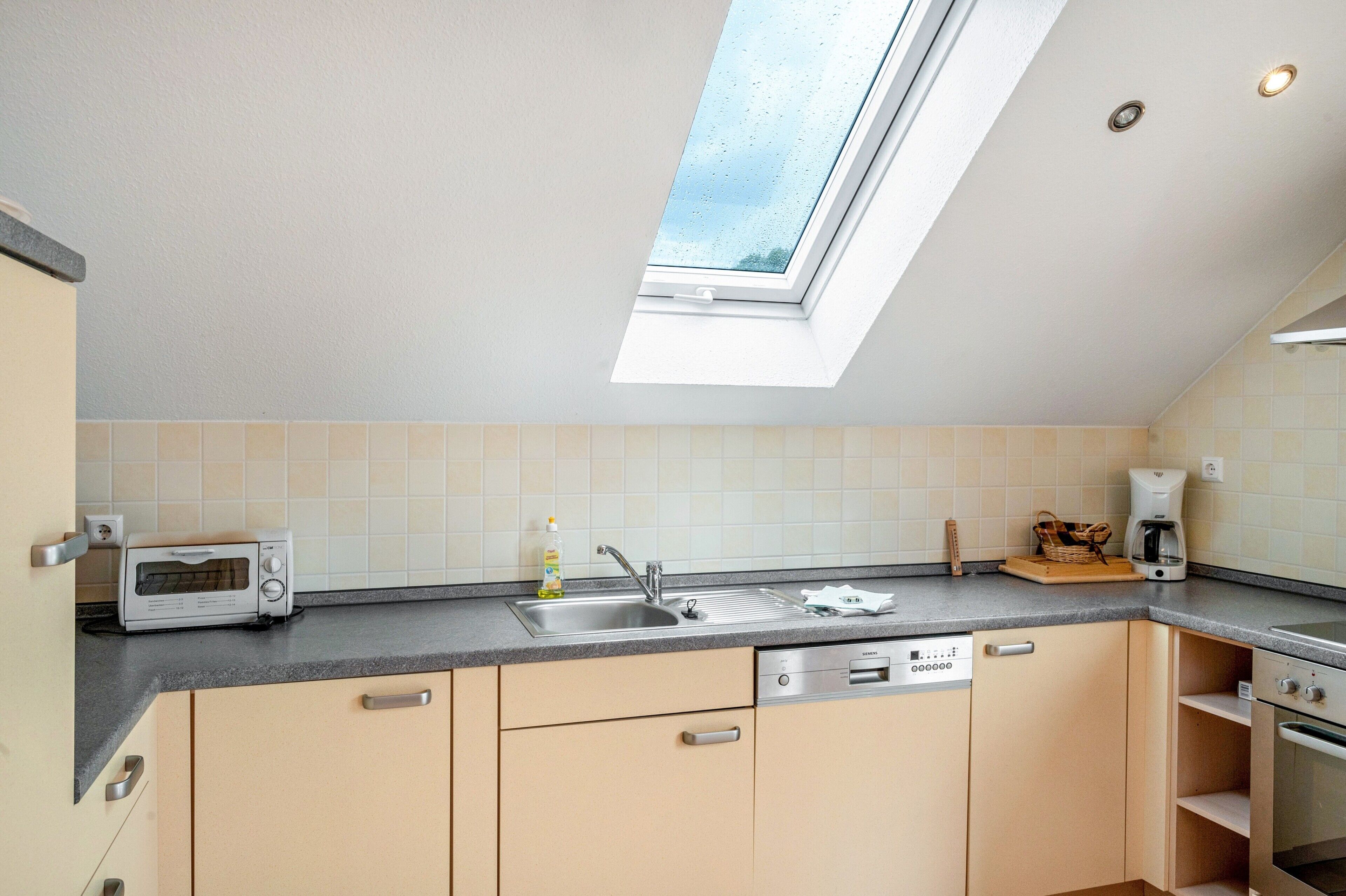 A kitchen with a skylight, a toaster, a sink, a dishwasher, and a coffee maker.
