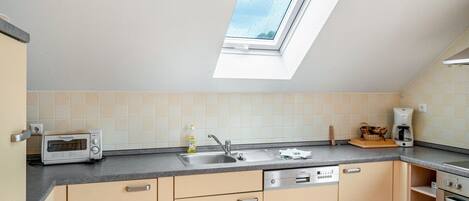 A kitchen with a skylight, a toaster, a sink, a dishwasher, and a coffee maker.