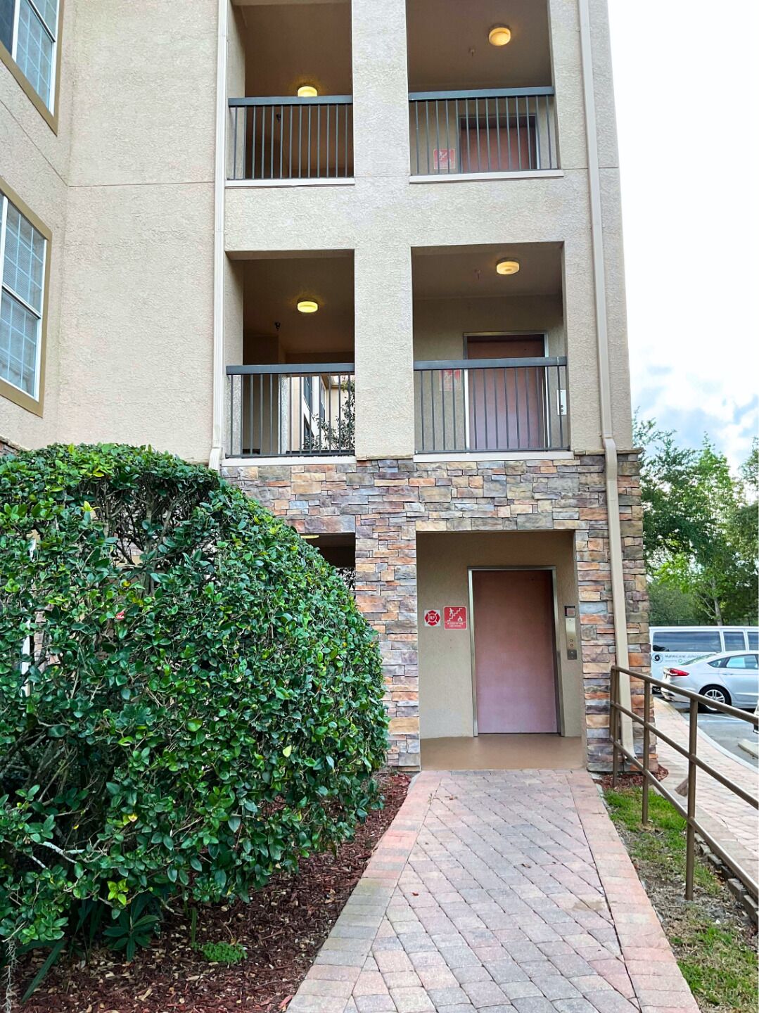 A multi-story building with a stone facade, a covered entrance, and a metal railing along the walkway.