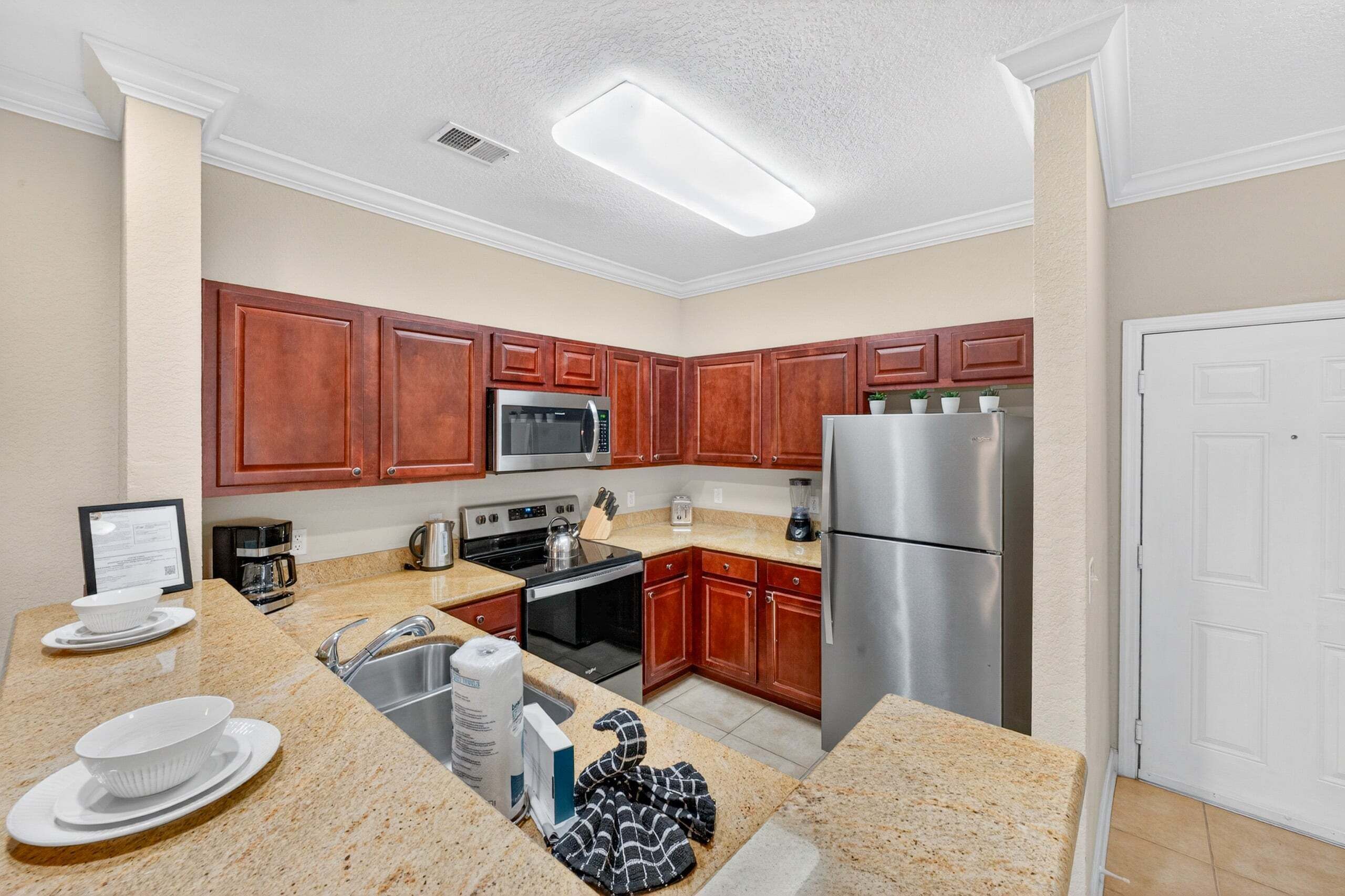 A compact kitchen with wooden cabinets, stainless steel appliances, granite countertops, and a white door.