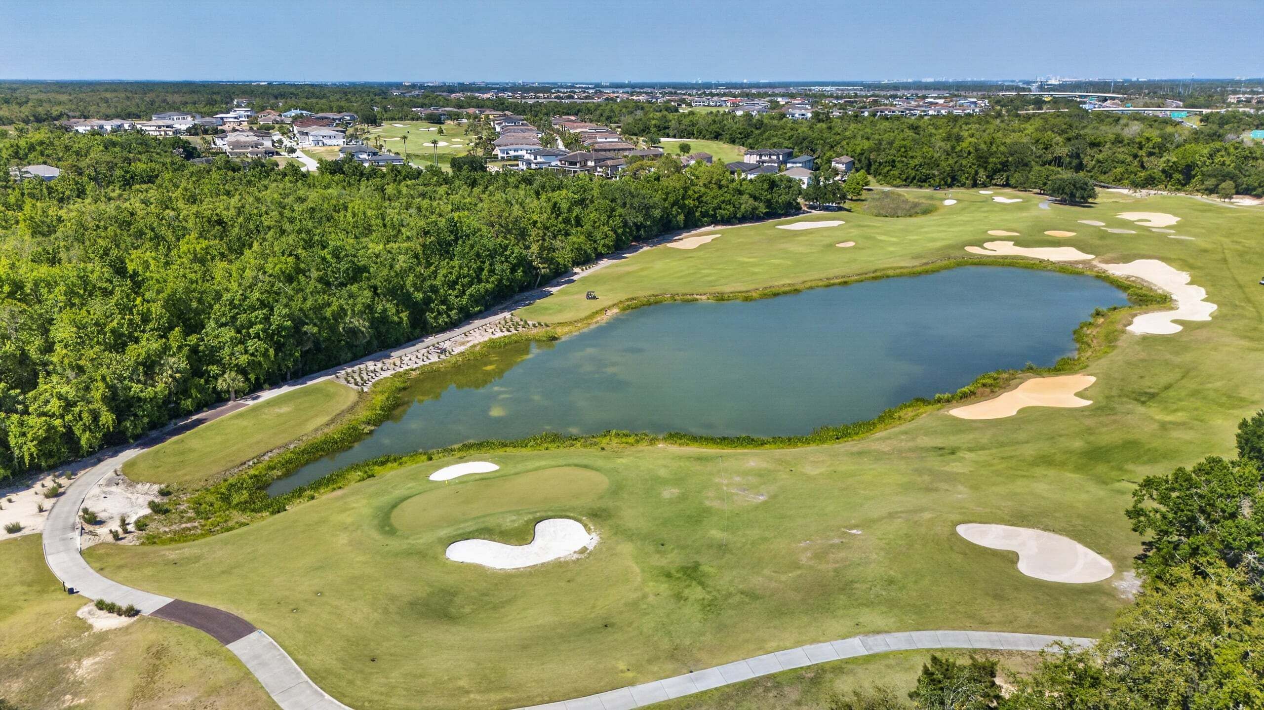 Un campo de golf con búnkeres de arena, un estanque y un bosque circundante.