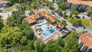 Luftaufnahme eines Resorts mit Schwimmbad, Liegebereichen und einem Parkplatz.
