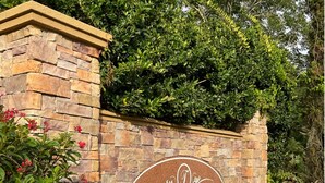 Eine Steinmauer mit einem Schild, auf dem 'TUSCANA ORLANDO'S MEDITERRANEAN INSPIRED GARDENS CONDOMINIUMS' steht.