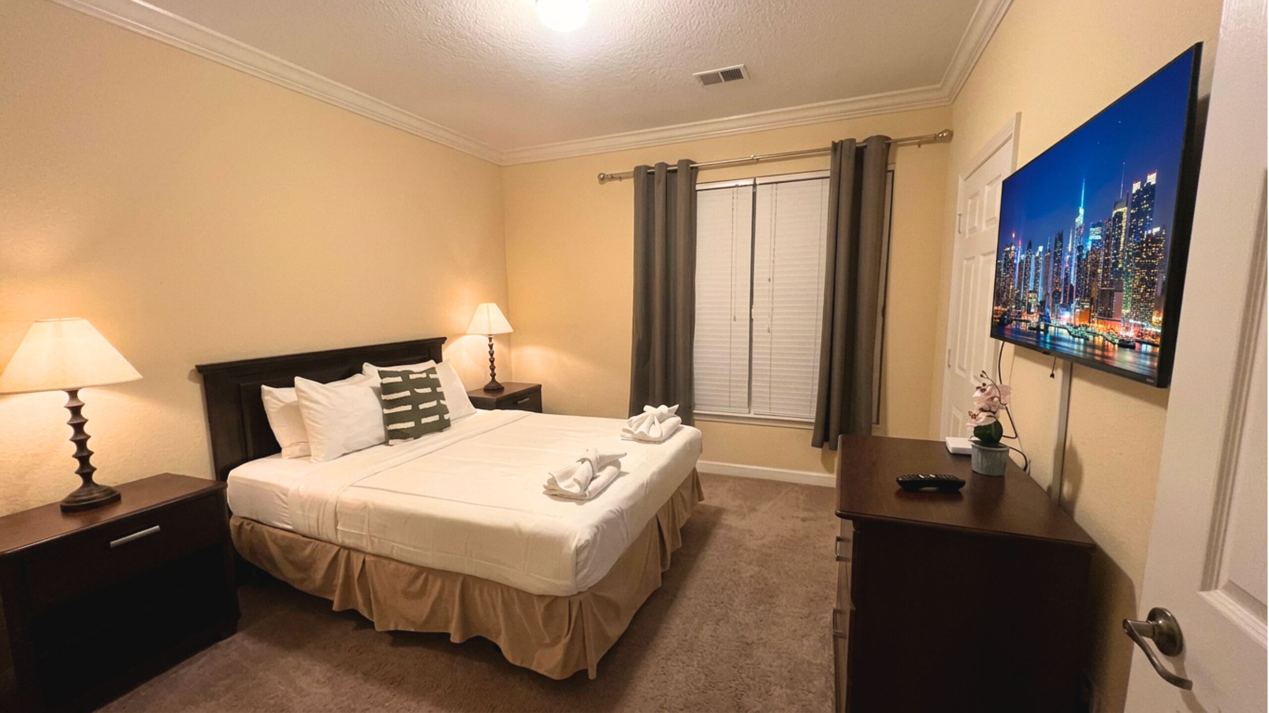 Habitación de hotel con cama, dos mesitas de noche, un escritorio, una silla, un cuadro y una ventana con cortinas.
