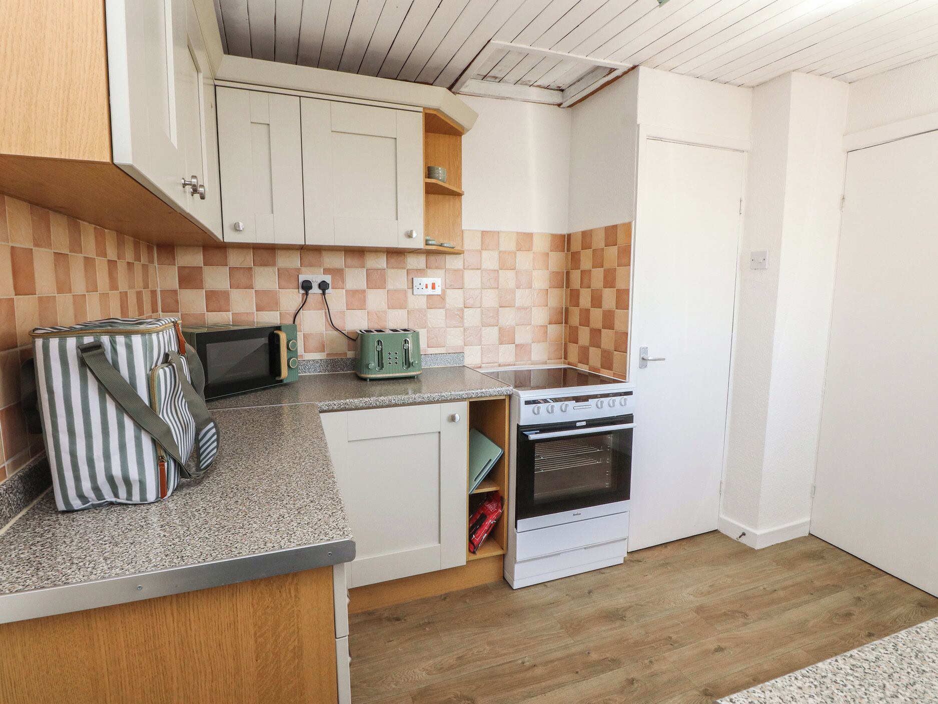 A compact kitchen with a microwave, toaster, and oven, wooden cabinets, and a checkered backsplash.