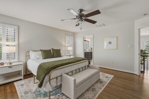 A bedroom with a bed, bedside table, lamp, bench, ceiling fan, windows, and a mirror.