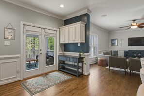 A spacious living area with a wooden floor, a gray sofa, a dark wooden console table, and a ceiling fan.
