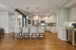 A kitchen with white cabinets, a stainless steel refrigerator, and a bar area with stools.