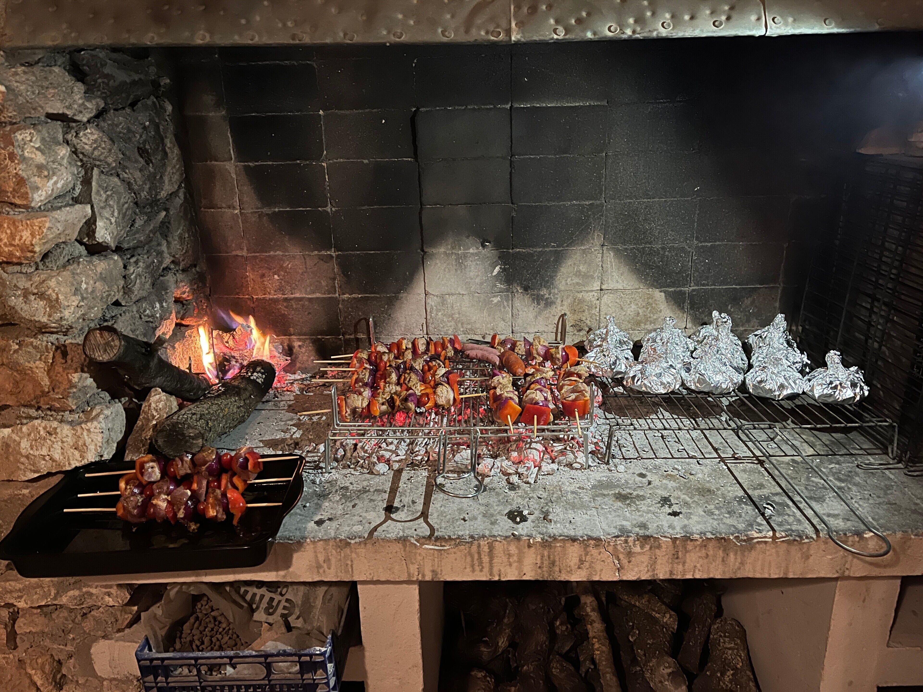 Un barbecue avec des brochettes de viande et de légumes, un feu et des aliments enveloppés dans du papier d’aluminium.