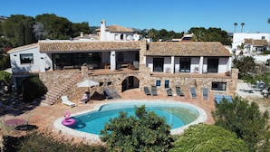 Uma casa de dois andares com piscina, paredes de pedra e uma varanda com espreguiçadeiras.