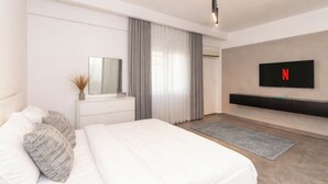 A modern bedroom with a bed, a dresser, a mirror, a TV mounted on the wall, and a large window with curtains. - Host Prime Boutique hotel 25 (New Cairo)