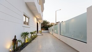 A modern building with a clean, white exterior, a paved walkway, and a row of potted plants along the side. - Host Prime Boutique hotel 25 (New Cairo)