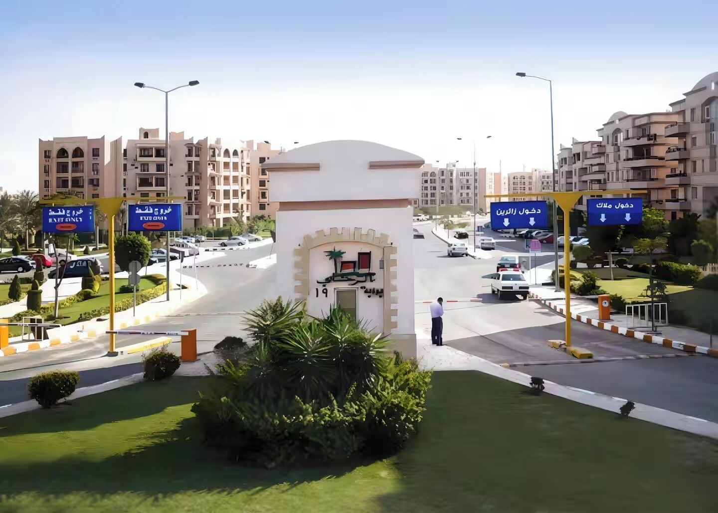 A gated entrance with a sign indicating 'Exit Only' and 'Entrance Only' directions, surrounded by greenery and modern buildings.