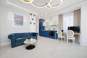 Una sala moderna con un sofá azul, una mesa de centro redonda y un televisor en la zona del comedor.