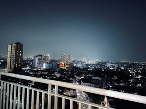 A nighttime cityscape with illuminated buildings and a balcony railing. - Grass Residence Cozy 1-bedroom condo with AC in awesome Quezon City (Quezon City)