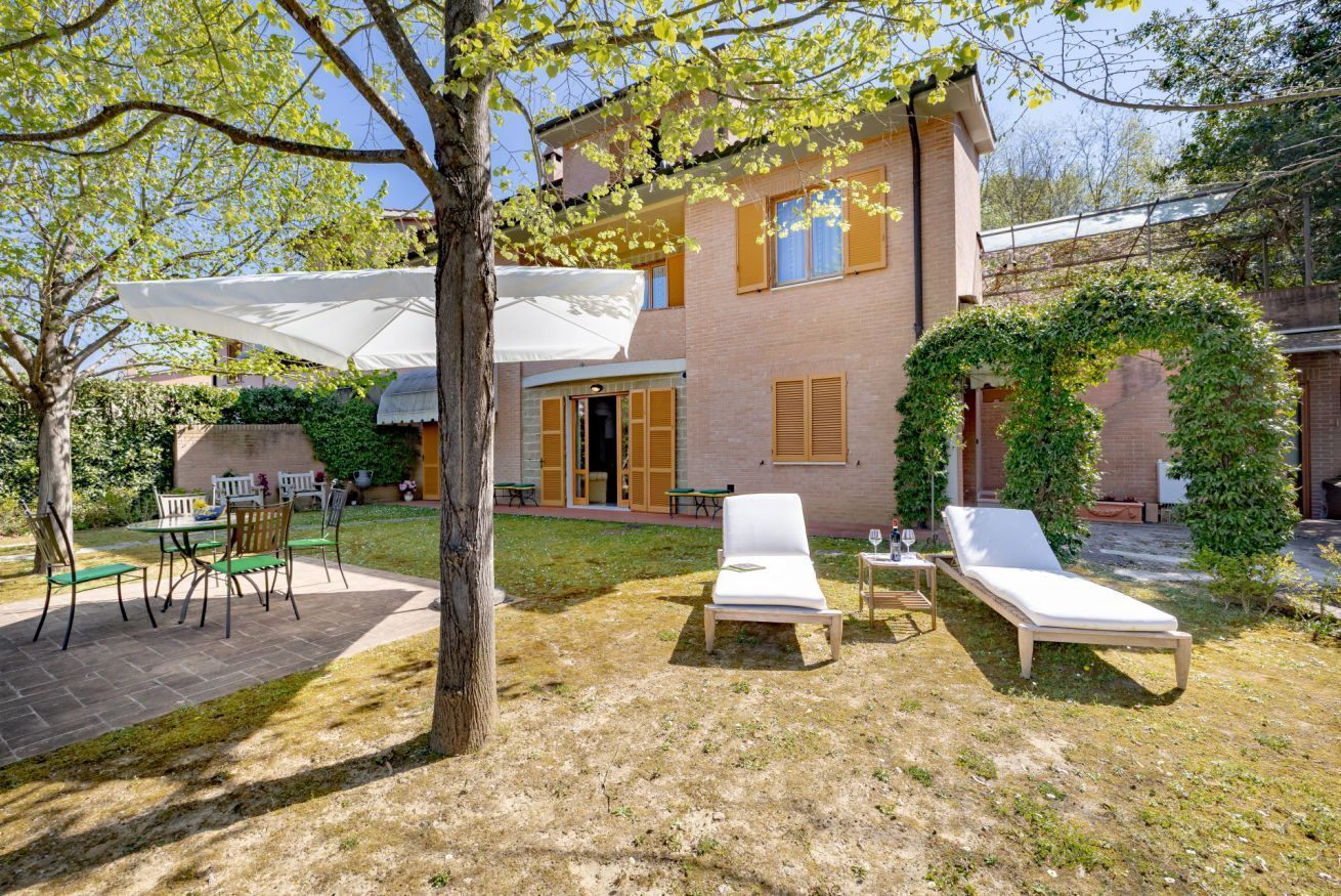 A two-story building with a patio area featuring a table, chairs, and lounge chairs.