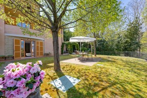 A building with a patio area, a tree, and a flower bed. - This cozy ground-floor apartment, ideal for 3 people, is perfect for a relaxing stay in Siena. The apartment overlooks the shared garden, where you can enjoy outdoor dining with a table, armchairs, and chairs with an umbrella. The location is convenient  (Siena)