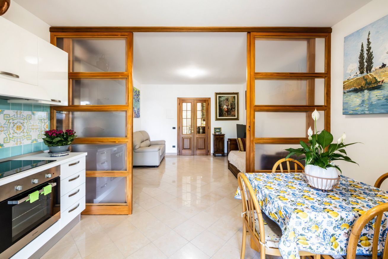 A kitchen with a stove, oven, and cabinets, a dining table with chairs, and a living area with a sofa and a painting.