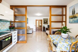 A kitchen with a stove, oven, and cabinets, a dining table with chairs, and a living area with a sofa and a painting. - This cozy ground-floor apartment, ideal for 3 people, is perfect for a relaxing stay in Siena. The apartment overlooks the shared garden, where you can enjoy outdoor dining with a table, armchairs, and chairs with an umbrella. The location is convenient  (Siena)