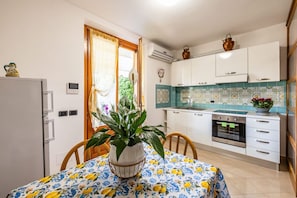 A compact kitchen with white cabinets, a built-in oven, and a dining area with a table set for two. - This cozy ground-floor apartment, ideal for 3 people, is perfect for a relaxing stay in Siena. The apartment overlooks the shared garden, where you can enjoy outdoor dining with a table, armchairs, and chairs with an umbrella. The location is convenient  (Siena)