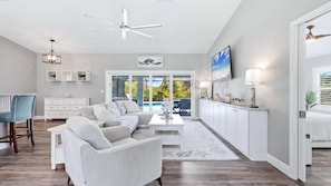 A modern living room with a sectional sofa, a ceiling fan, a TV, and a view of the outdoors. - Welcome to Villa Sunrise, 3 king bedrooms, pool and gas firepit table (Englewood)