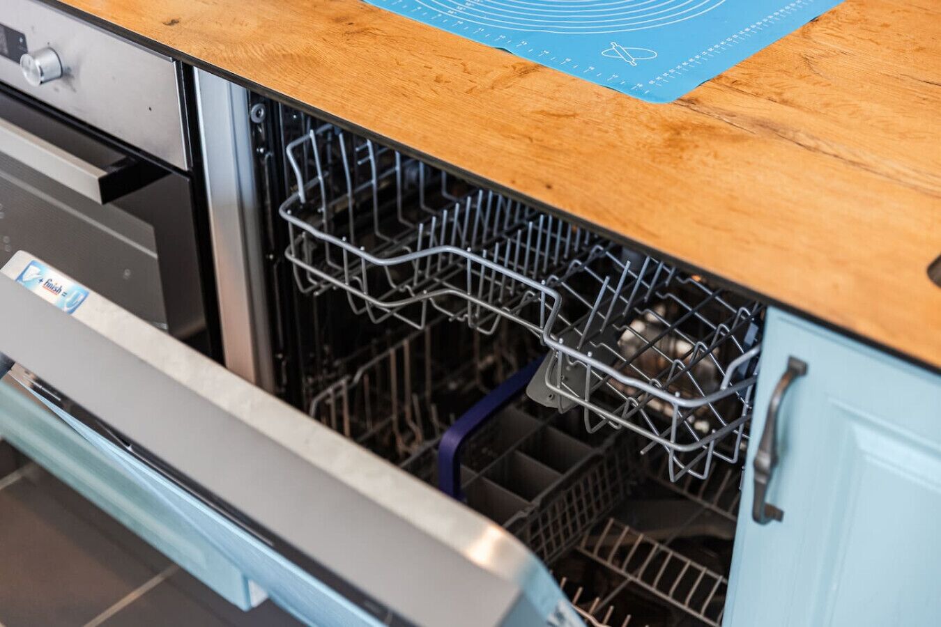 An open dishwasher with a blue mat on the countertop.