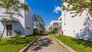 En bostadsgata med vita hus, en kullerstensbelagd gång och grönskande gräsmattor.