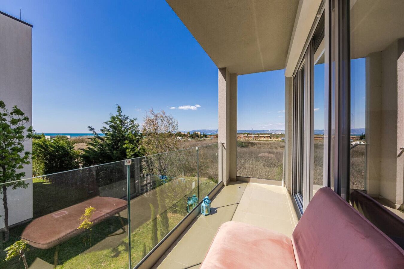 A balcony with a view of the sea, a glass railing, and a bench.