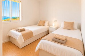 Quarto com duas camas, mesa de cabeceira, janela com vista e luminária na parede.