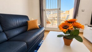A living room with a dark blue sofa, a single orange cushion, a white coffee table, and a potted sunflower plant. - Casa Miramar | Beach, Pool & Terrace in Mojácar Playa (Mojácar)