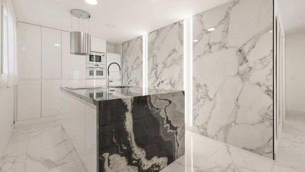 A modern kitchen with white cabinets, a black marble island, and a stainless steel range hood.