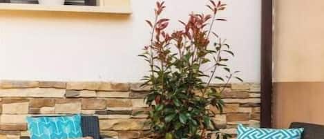 Un espacio al aire libre con mobiliario de mimbre, una pared de piedra y una planta en maceta.