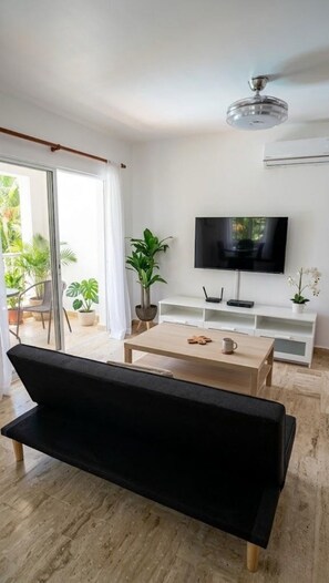 En moderne stue med en sort sofa, et træbord, et fjernsyn og en potteplante.