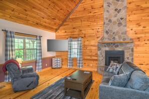 Ein gemütliches Blockhaus mit Holzwänden, einem Steinkamin, einer bequemen Couch, einem Relaxsessel und einem Flachbildfernseher.