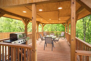 Eine Holzterrasse mit Grill, Tisch, Stühlen und Blick auf Bäume.