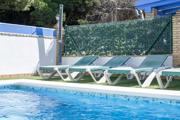 Ein Pool mit Liegestühlen, einer Ziegelwand und einem grünen Zaun.