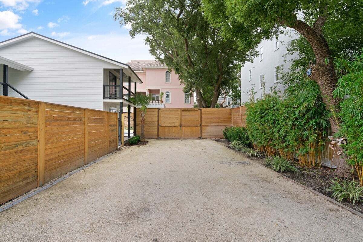 Un quartier résidentiel avec une allée en gravier, une clôture en bois et un grand arbre.