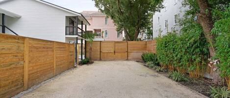 Un quartier résidentiel avec une allée en gravier, une clôture en bois et un grand arbre.
