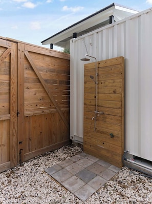 A wooden door with a shower, a white container, and a gravel path.