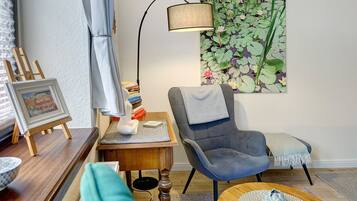 Ett rum med en stol, ett bord, en lampa, en liten tavla och en vägg med blommig tapet.