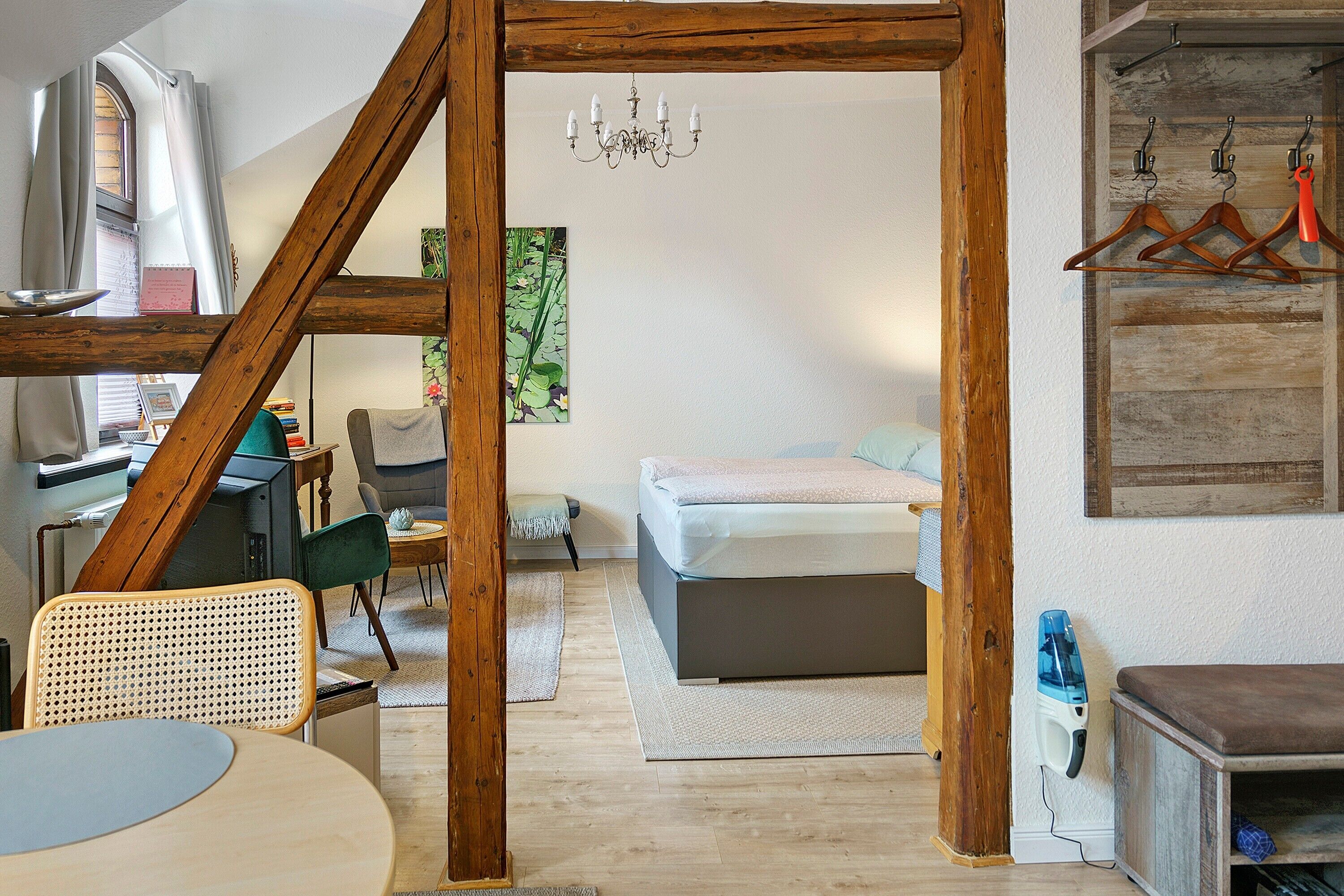 Quarto com cama, escrivaninha, cadeira, luminária pendente e um cabideiro.