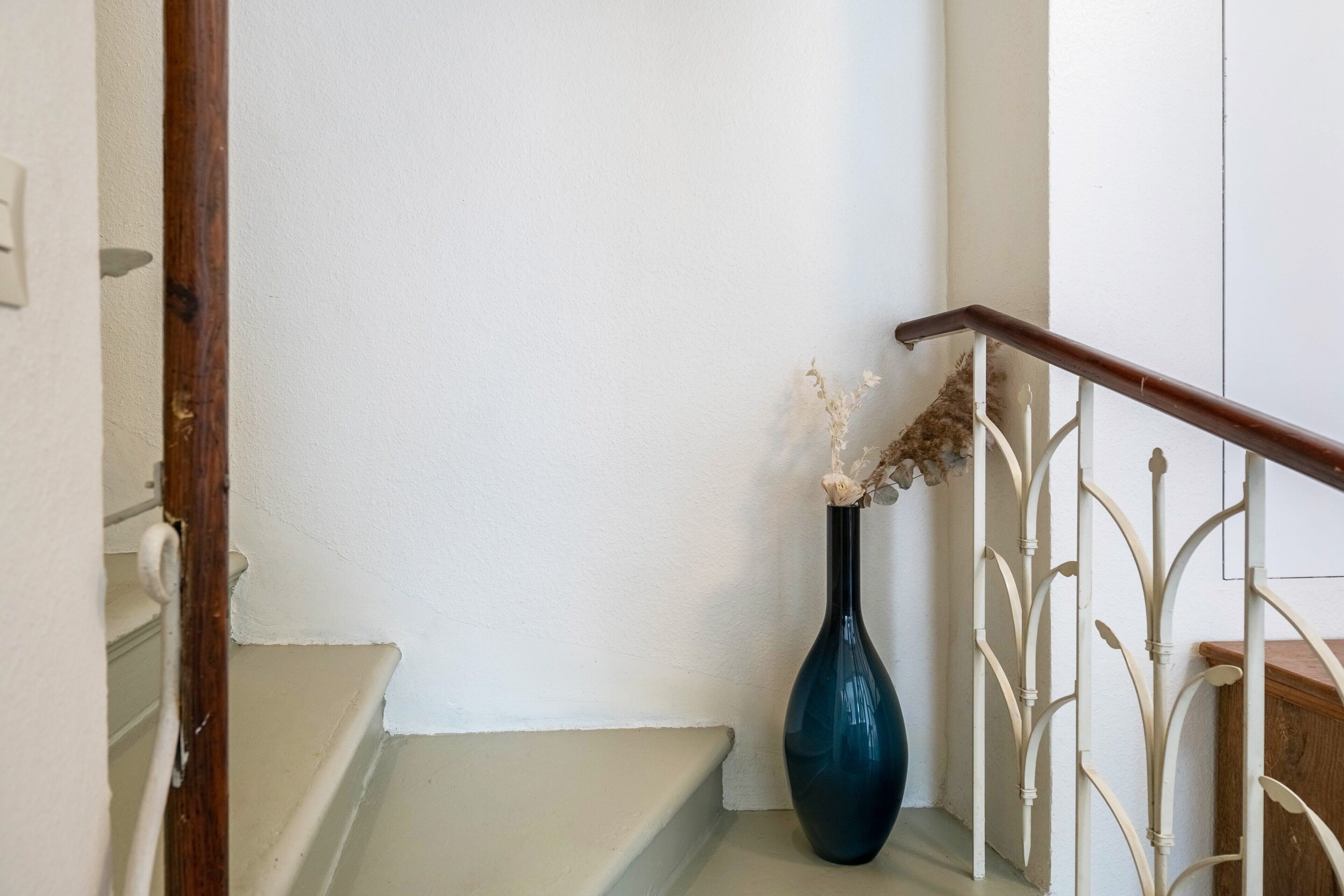 A staircase with a white railing and a dark blue vase with dried flowers on the landing.