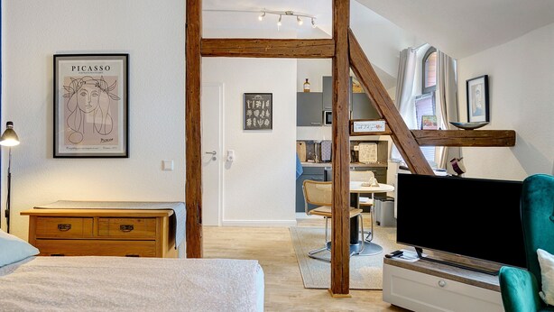 Ein modernes Schlafzimmer mit einem Holz-Kopfteil, einem Flachbildfernseher, einem grünen Sessel und einem Essbereich mit Holztisch und Stühlen.