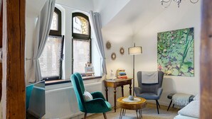 Ein Wohnzimmer mit einem blaugrünen Sessel, einem grauen Sessel, einem runden Holztisch, einer Stehlampe und einem Gemälde von Seerosen.