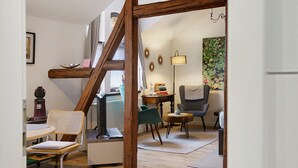 Ein Zimmer mit einer Holztreppe, einem Schreibtisch mit Computer, einem Stuhl, einer Lampe und einem Gemälde an der Wand.