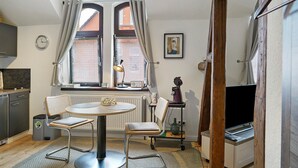 Ein kompakter Wohnbereich mit Esstisch, zwei Stühlen, Fernseher, Heizkörper und einem fenster mit Vorhängen.