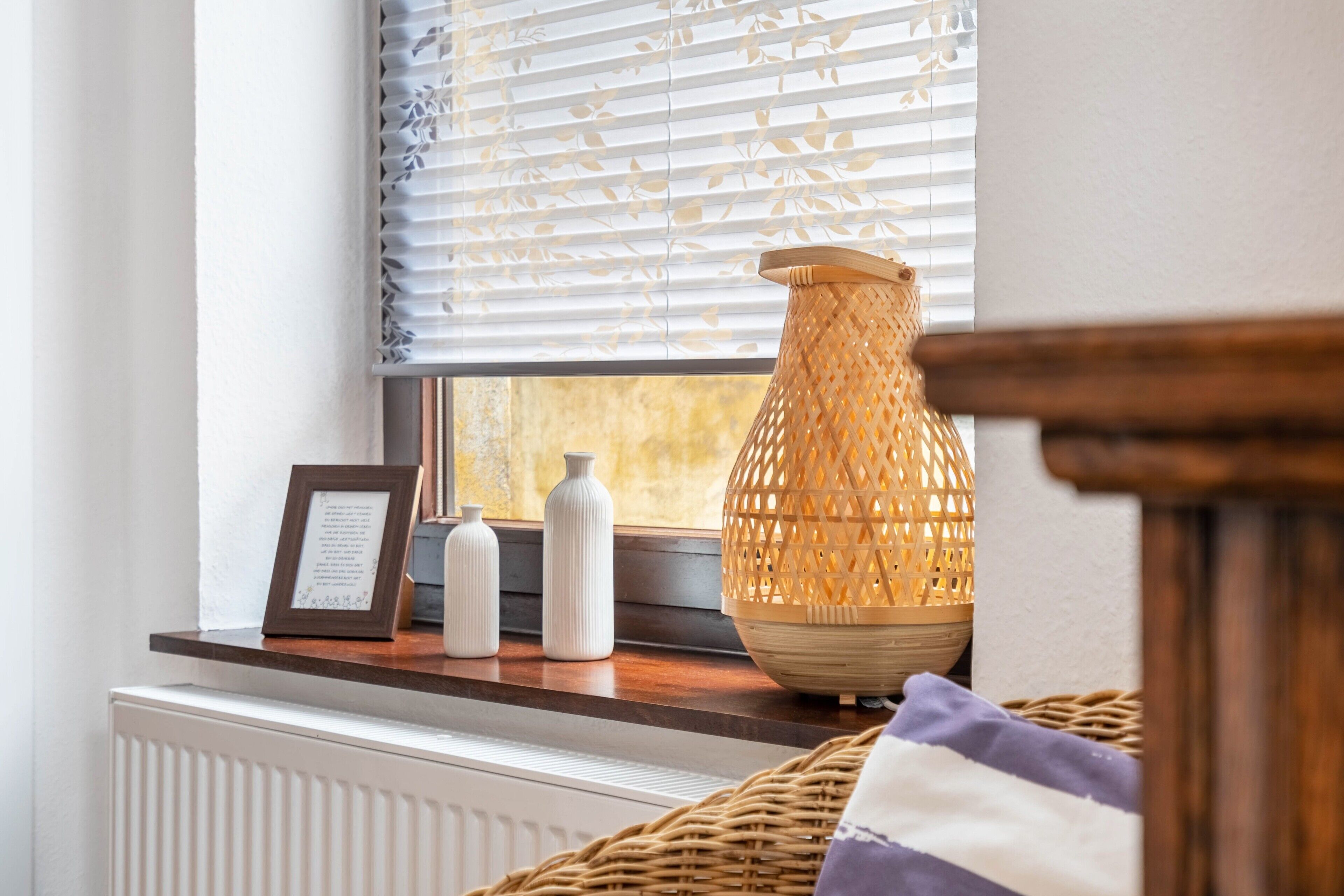 A window with a wicker basket, a framed picture, and two bottles on a wooden ledge.