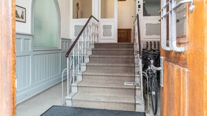 Uma escadaria com corrimão de madeira, uma porta branca e uma bicicleta estacionada ao lado.