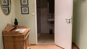Une commode en bois avec une petite plante, une salle de bain avec un lavabo et un miroir, et une porte donnant sur une autre pièce.