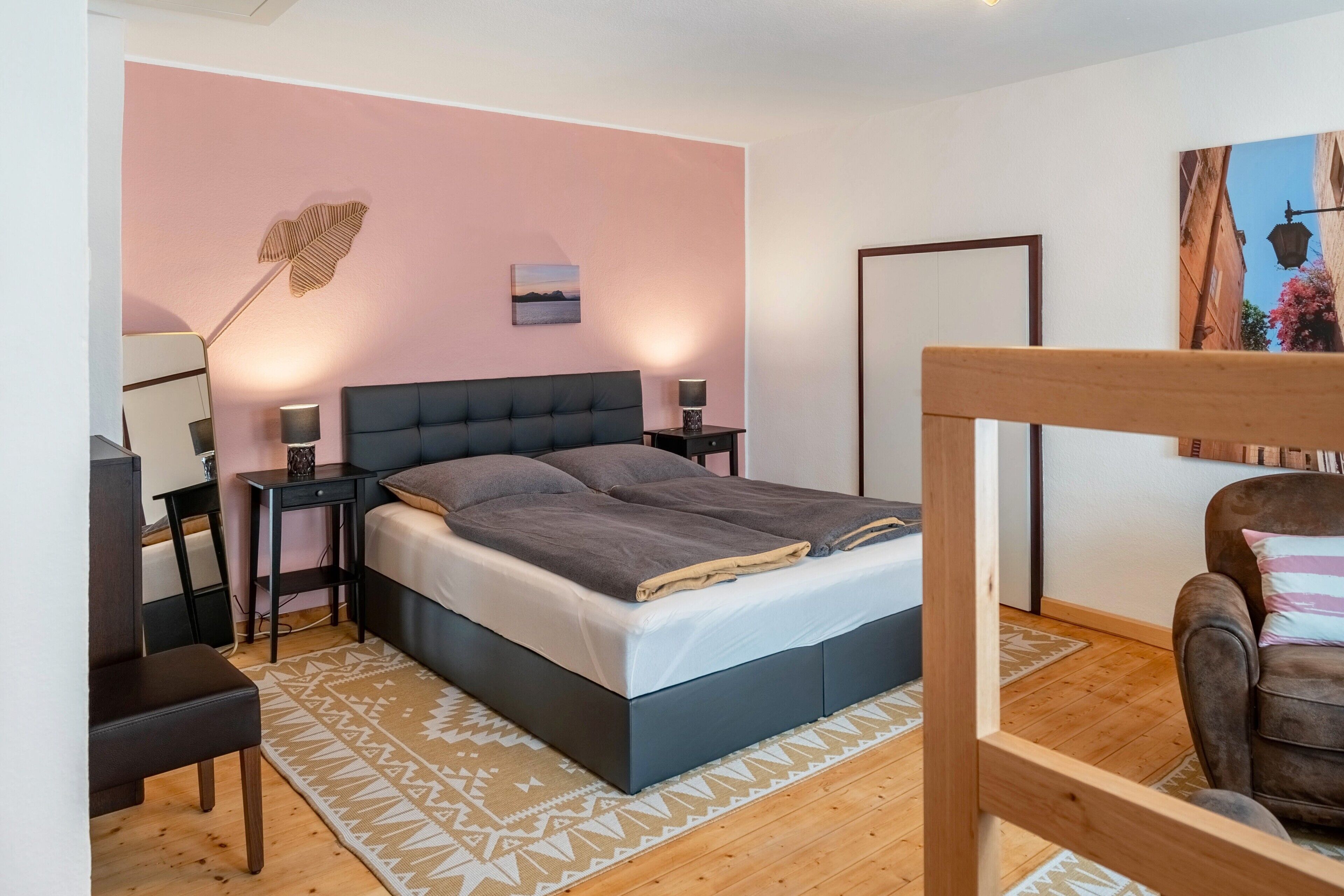 A bedroom with a bed, bedside tables, a chair, a rug, and a painting on the wall.